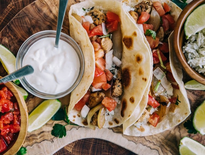 An olive board filled with delicious mexican fiesta of food tacos and burritos with cheese, onions, chicken, pico de gallo, cilantro lime rice and sour cream