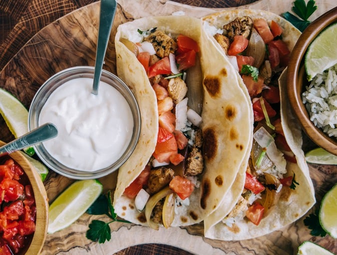 An olive board filled with delicious mexican fiesta of food tacos and burritos with cheese, onions, chicken, pico de gallo, cilantro lime rice and sour cream