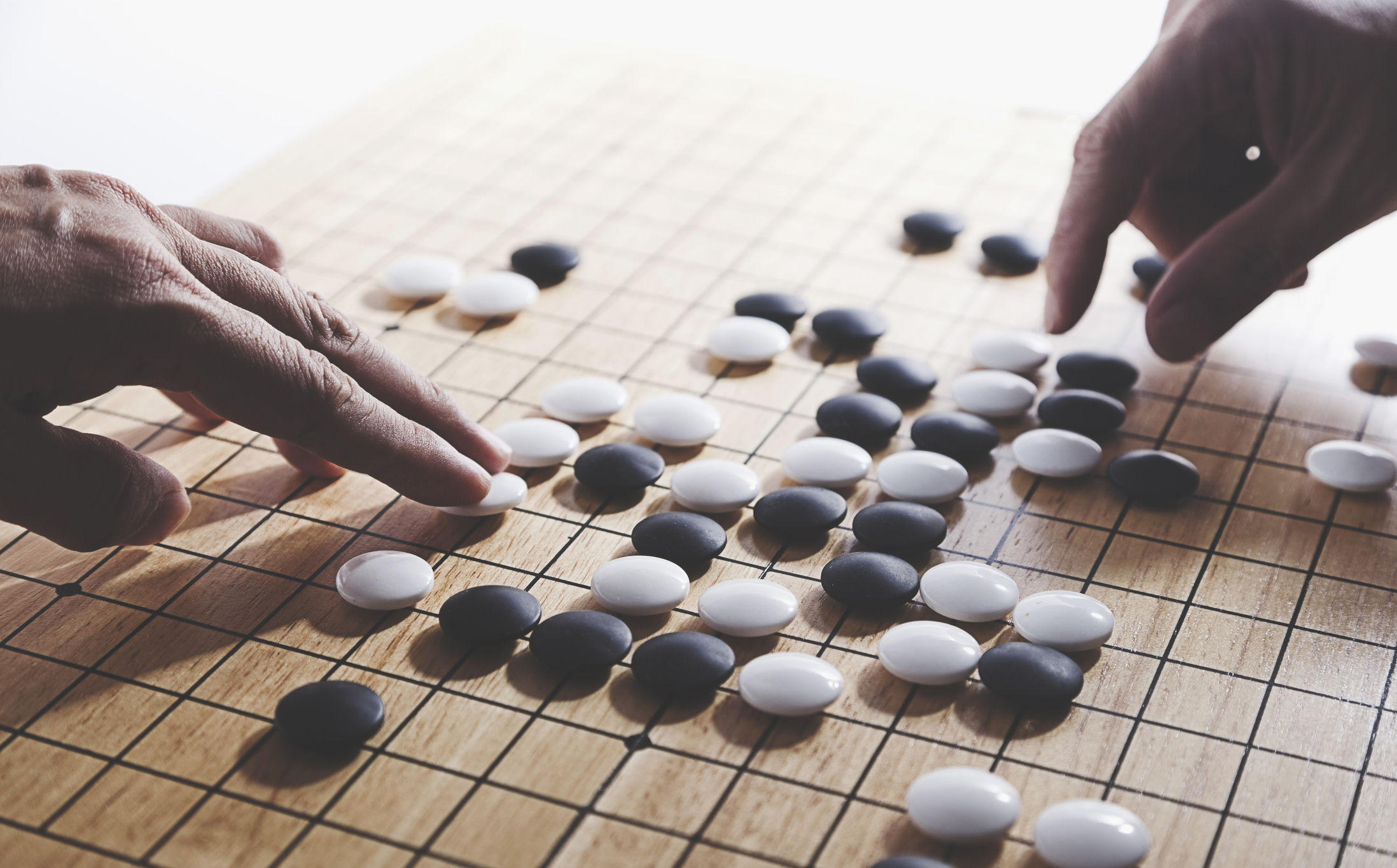 Två spelares händer som spelar brädspelet Go